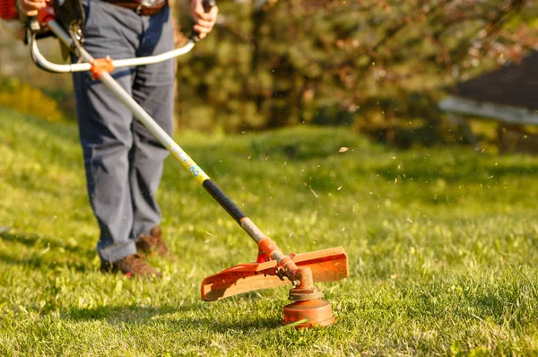 Klipptrimmer - arbetare klipper gräs på grön gård vid solnedgången — Stockfoto