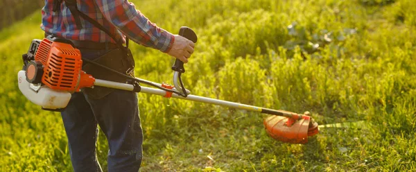 Mowing trimmer - worker cutting grass in green yard at sunset — Stock Photo, Image