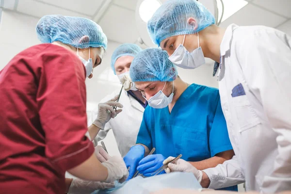 Grupo de cirujanos trabajando en quirófano. Equipo de medicina de reanimación con máscaras protectoras que sostienen herramientas médicas de acero —  Fotos de Stock