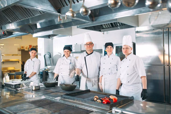 Cinque chef che indossano uniformi in posa in cucina. — Foto Stock