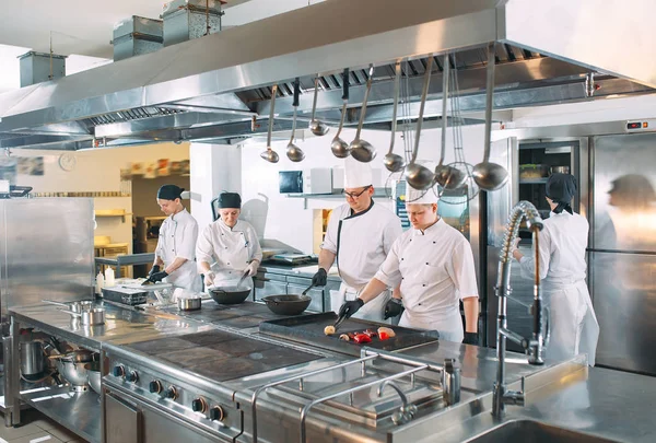 Cinco chefs vestindo uniformes posando em uma cozinha. — Fotografia de Stock
