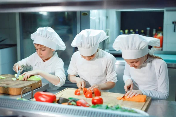 Children in chefs hat grind vegetables on the kitchen. — Stock Photo, Image