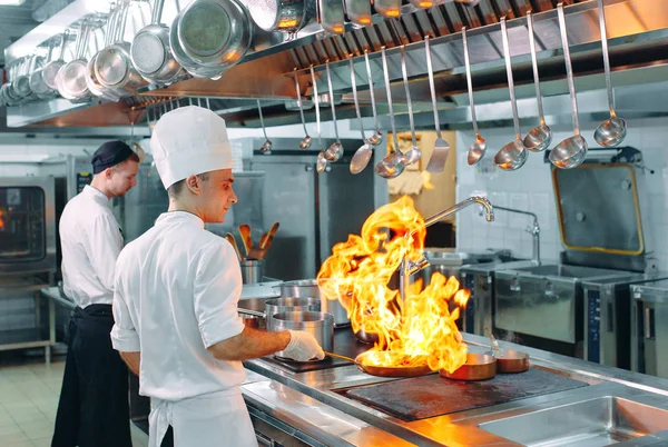 Modernt kök. Matlagare lagar mat på spisen i köket i restaurangen eller hotellet. Branden i köket. — Stockfoto