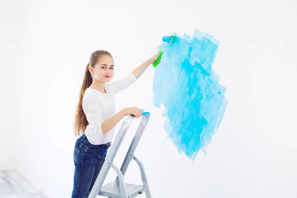 Repair in the apartment. Happy child girl paints the wall with blue paint, — Stock Photo, Image