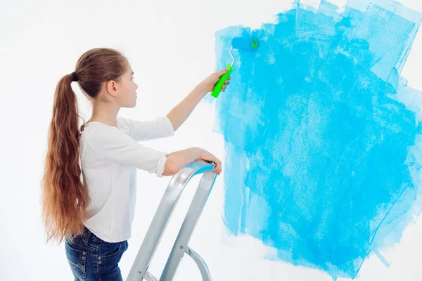 Repair in the apartment. Happy child girl paints the wall with blue paint, — Stock Photo, Image