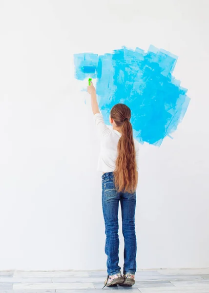 Reparación en el apartamento. Niña feliz pinta la pared con pintura azul, — Foto de Stock