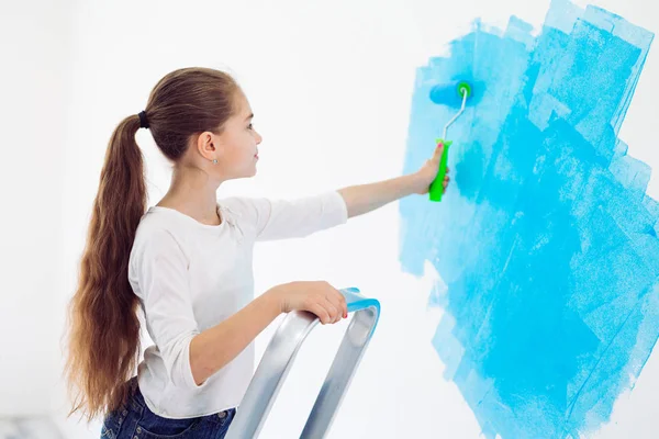 Repair in the apartment. Happy child girl paints the wall with blue paint, — Stock Photo, Image