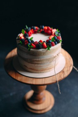 Meyveli kek. Kek, siyah arka plandaki ahşap bir stantta böğürtlenlerle süslenmiş..