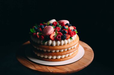 Meyveli kek. Kek, siyah arka plandaki ahşap bir stantta böğürtlenlerle süslenmiş..