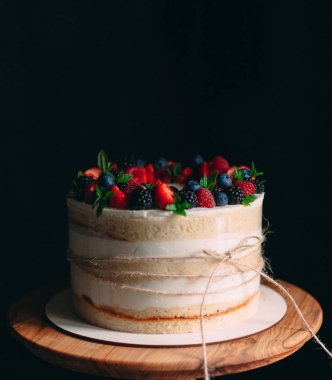 Meyveli kek. Kek, siyah arka plandaki ahşap bir stantta böğürtlenlerle süslenmiş..