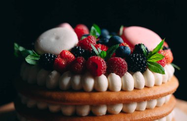 Meyveli kek. Kek, siyah arka plandaki ahşap bir stantta böğürtlenlerle süslenmiş..