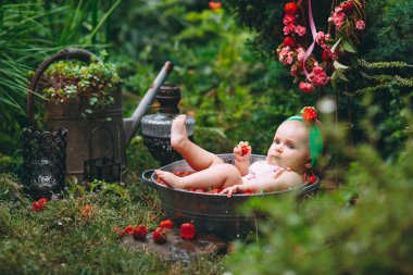 A little girl bathes in a basin with strawberries in the garden. clipart