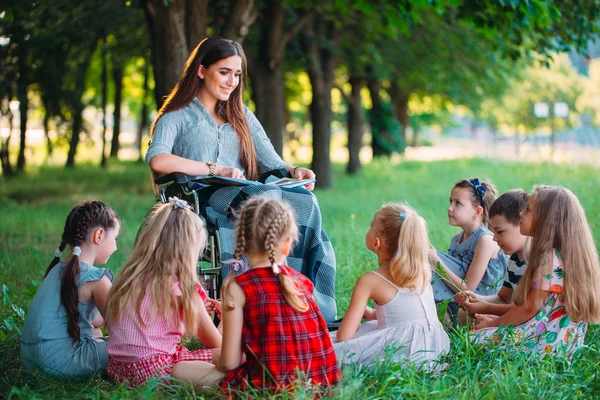 Enseignant handicapé mène une leçon avec les enfants dans la nature. Interaction d'un enseignant en fauteuil roulant avec des élèves. — Photo