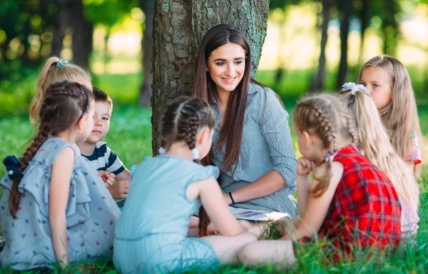 Enfants et éducation, jeune femme au travail comme éducatrice lisant un livre aux garçons et aux filles du parc. — Photo