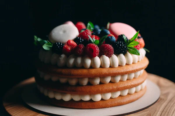 Fruit cake. Cake decorated with berries on a wooden stand on a black background. — Stock Photo, Image