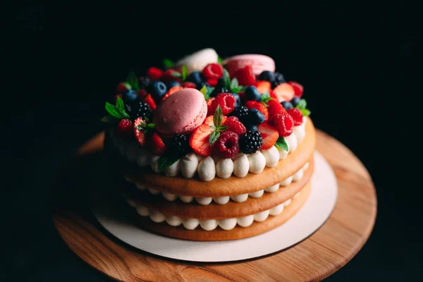 Fruit cake. Cake decorated with berries on a wooden stand on a black background. — Stock Photo, Image