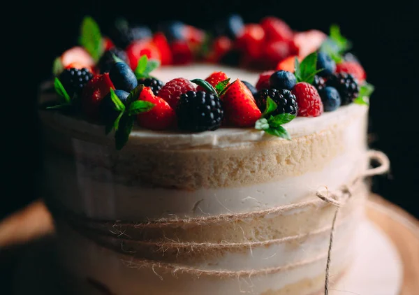 Fruit cake. Cake decorated with berries on a wooden stand on a black background. — Stock Photo, Image