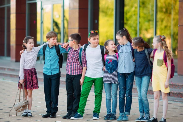 Amistad infantil. Estudiantes de la escuela se paran en un abrazo en el patio de la escuela. — Foto de Stock