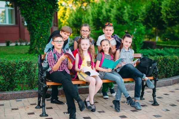 Happy Schoolmates Portrait. Schoolmates seating with books in a wooden bench in a city park and studying on sunny day. — Stock Photo, Image