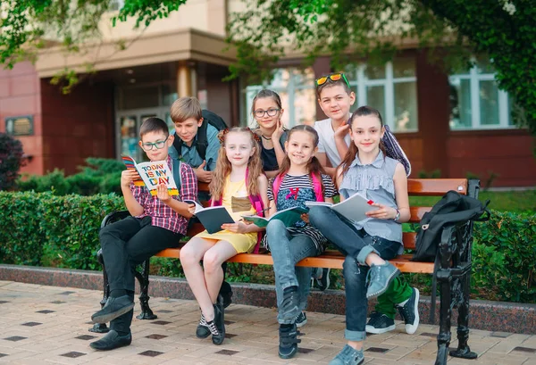 Happy Schoolmates Portrait. Schoolmates seating with books in a wooden bench in a city park and studying on sunny day. — Stock Photo, Image