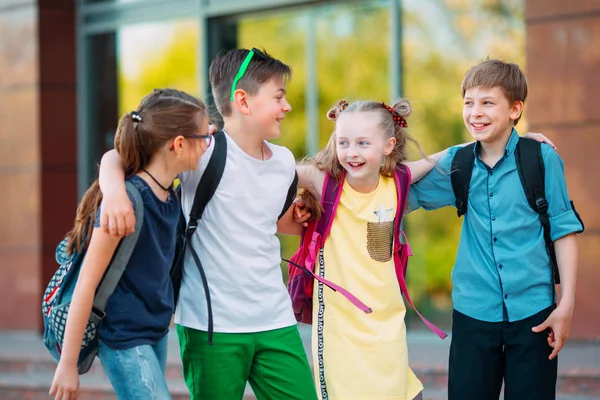 Παιδική φιλία. Τέσσερις μικροί μαθητές, δύο αγόρια και δύο κορίτσια, στέκονται σε μια αγκαλιά στην αυλή του σχολείου. — Φωτογραφία Αρχείου