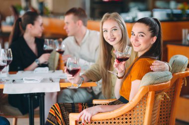 Arkadaşlar şarap içerek, konuşarak ve gülümseyerek eğlenirler..