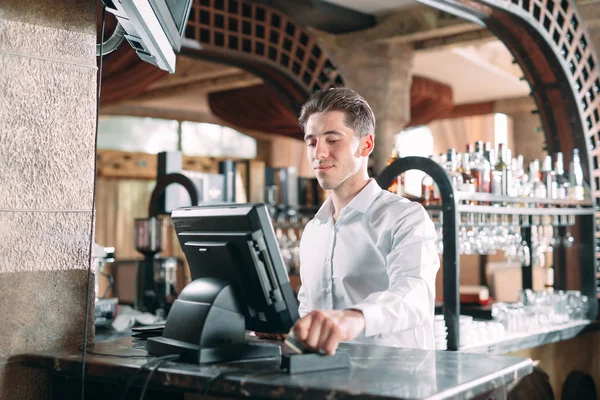 Kisvállalkozás, emberek és szolgáltatás koncepció - boldog ember vagy pincér kötényben a pultnál pénztárgéppel dolgozik a bárban vagy kávézóban. — Stock Fotó