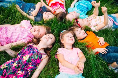 Parktaki yeşil çimlerin üzerinde yatan bir grup çocuk. Çocukların etkileşimi....