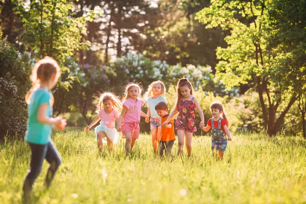 Duża grupa dzieci, przyjaciół chłopców i dziewcząt biegających w parku w słoneczny letni dzień w luźnych ubraniach . — Zdjęcie stockowe