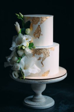 Siyah arka planda, ahşap bir stantta çiçekli iki katlı bir pasta..