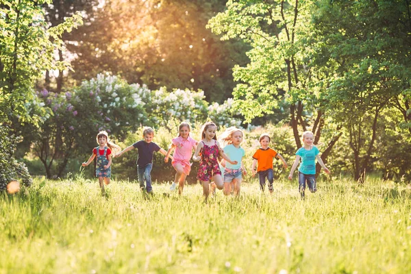 Duża grupa dzieci, przyjaciół chłopców i dziewcząt biegających w parku w słoneczny letni dzień w luźnych ubraniach . — Zdjęcie stockowe