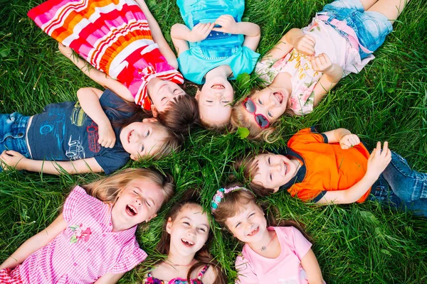 Група дітей лежить на зеленій траві в парку. Взаємодія дітей . — стокове фото