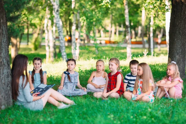 Діти та освіта, молода жінка на роботі як педагог читає книгу для хлопчиків та дівчаток у парку . — стокове фото