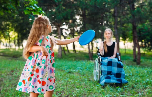 Una joven discapacitada juega al frisbee con su hermana menor. Interacción de una persona sana con una persona con discapacidad —  Fotos de Stock