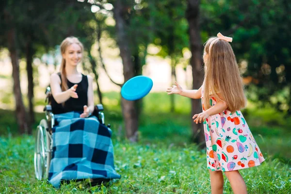 Una joven discapacitada juega al frisbee con su hermana menor. Interacción de una persona sana con una persona con discapacidad —  Fotos de Stock