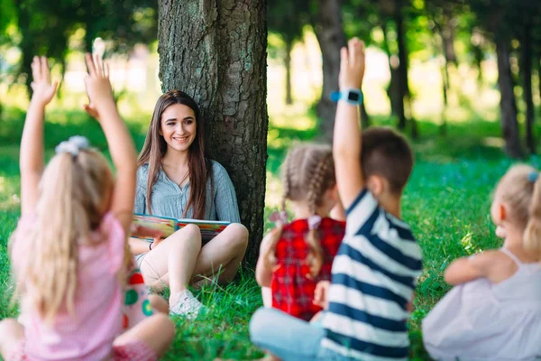 Niños y educación, mujer joven en el trabajo como educadora leyendo libro para niños y niñas en el parque. —  Fotos de Stock