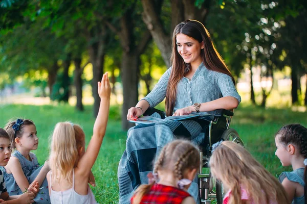Enseignant handicapé mène une leçon avec les enfants dans la nature. Interaction d'un enseignant en fauteuil roulant avec des élèves. — Photo
