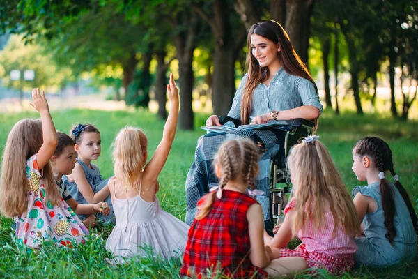 Profesor discapacitado lleva a cabo una lección con los niños en la naturaleza. Interacción de un profesor en silla de ruedas con los estudiantes. —  Fotos de Stock