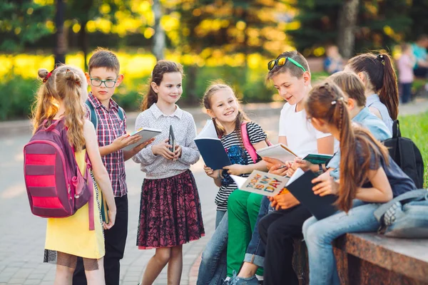 Boldog iskolatársak portréja. Iskolatársak ülnek könyvek egy fa padon a városi parkban, és tanul a napsütéses napon. — Stock Fotó