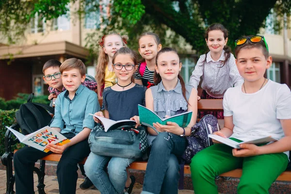 Feliz retrato de compañeros de escuela. Compañeros de escuela sentados con libros en un banco de madera en un parque de la ciudad y estudiando en un día soleado. —  Fotos de Stock