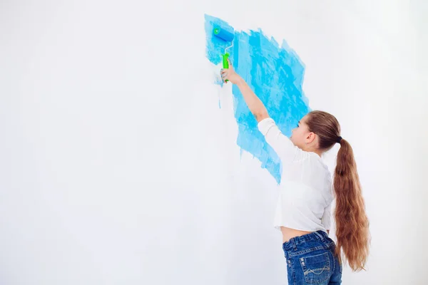 Repair in the apartment. Happy child girl paints the wall with blue paint, — Stock Photo, Image