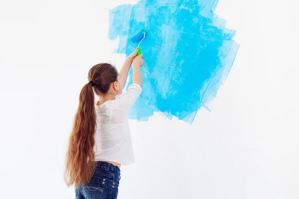 Reparación en el apartamento. Niña feliz pinta la pared con pintura azul, — Foto de Stock