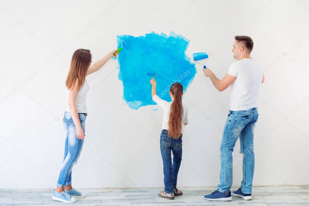 Mother, father and little daughter painting the wall in their new home.