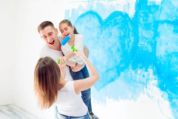Matka, otec a dcera malují zeď v novém domově. — Stock fotografie