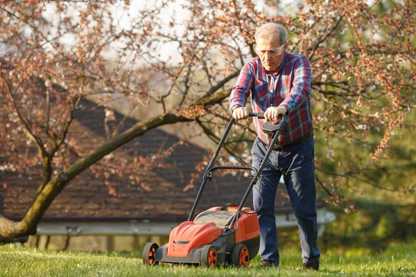 Man met elektrische grasmaaier, grasmaaier. Tuinman snoeit een tuin. Zonnige dag, buitenwijk, dorp. Volwassen man snoeien en landschapsarchitectuur tuin, trimmen gras, gazon, paden. Hard werken aan de natuur. — Stockfoto