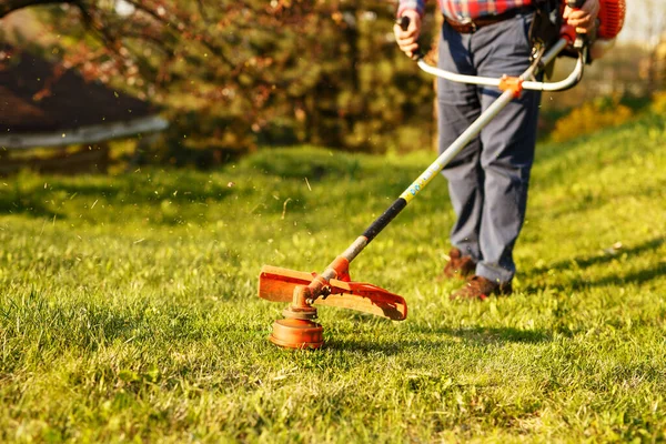Aparador de corte - trabalhador cortar grama no quintal verde ao pôr do sol — Fotografia de Stock
