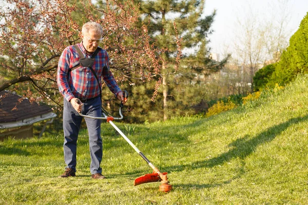 Maaimachine - werknemer maait gras in groene tuin bij zonsondergang — Stockfoto