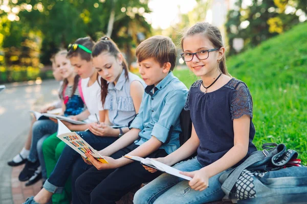 Feliz retrato de compañeros de escuela. Compañeros de escuela sentados con libros en un banco de madera en un parque de la ciudad y estudiando en un día soleado. —  Fotos de Stock