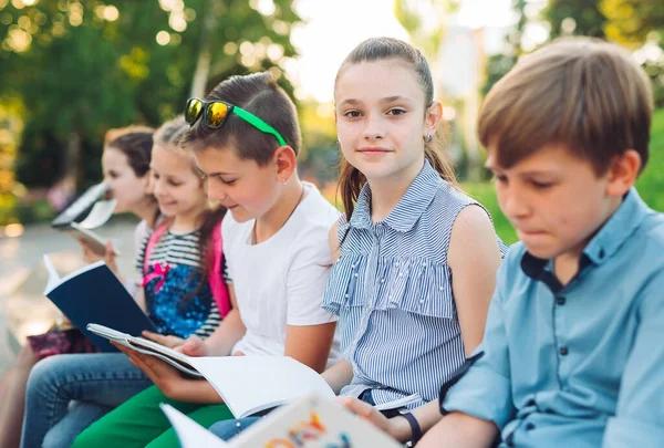 Buon Ritratto dei compagni di scuola. Compagni di scuola seduti con libri in una panchina di legno in un parco cittadino e che studiano nelle giornate di sole. — Foto Stock