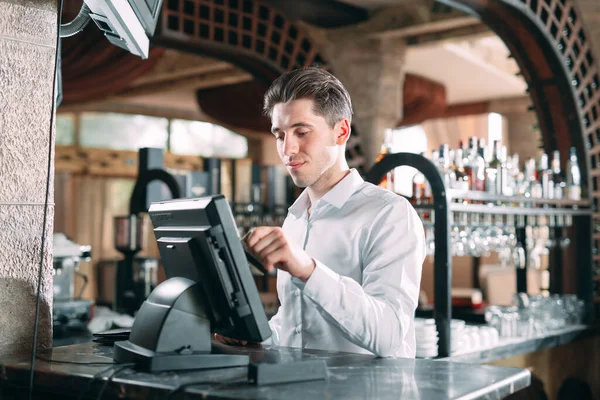 Conceito de pequenas empresas, pessoas e serviços - homem feliz ou garçom em avental no balcão com caixa de dinheiro trabalhando no bar ou café. — Fotografia de Stock